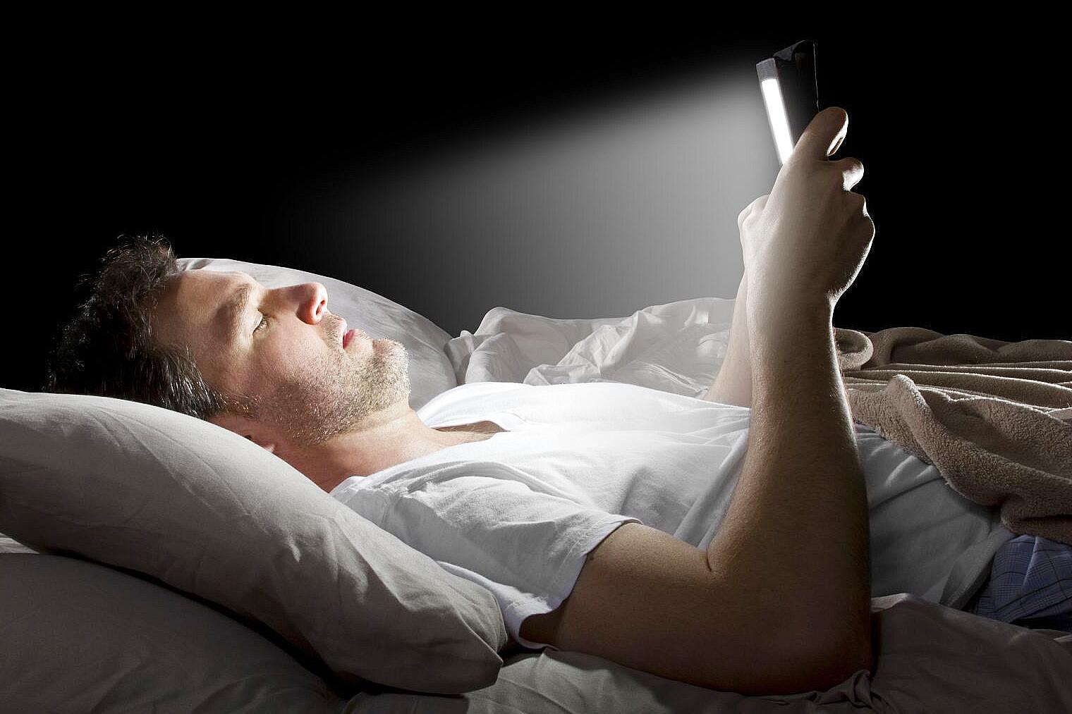 Adult using smartphone in bed at night with screen light causing tiredness